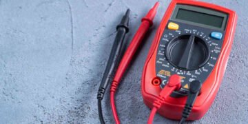 Red multimeter or a multitester, also known as a VOM on gray table. Electronic measuring instrument. Red and black wires